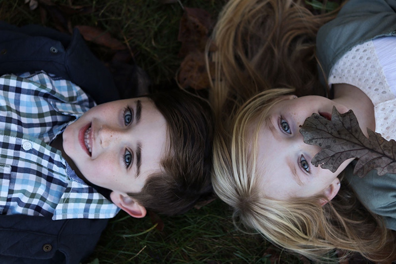 Two girls lie on a pile of fall leaves