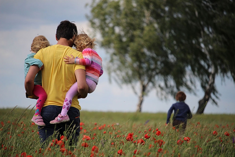 A father carries two of his children while another runs ahead