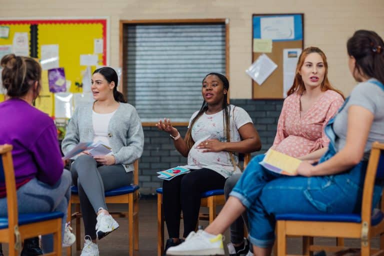 An over the shoulder view of a group of pregnant women who are sharing their journey together. They are attending a pregnancy group and fitness class in a community centre in the North East of England. They are discussing the classes they will be taking.