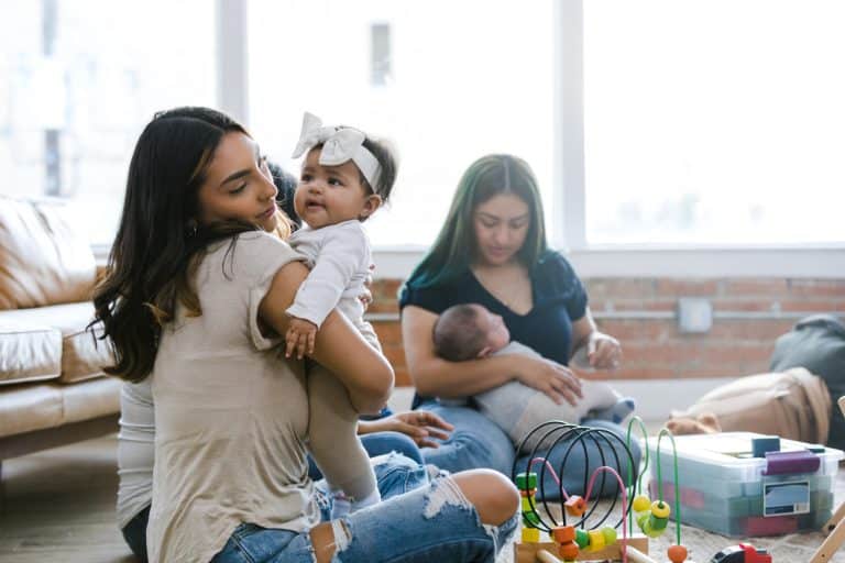 Smiling women with infants enjoying togetherness and support in a home setting.