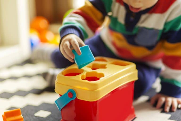 A faceless shot of a toddler placing a block in a box with shape cutouts.